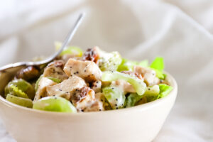 Close up of chicken salad in bowl showing cubes of chicken, halved grapes and celery slices in a creamy dressing with poppy seeds.