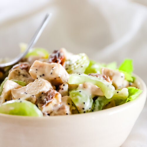 Close up of chicken salad in bowl showing cubes of chicken, halved grapes and celery slices in a creamy dressing with poppy seeds.