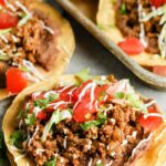 Tostadas topped with ground beef, tomato chunks and crema drizzled over.