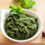 Closeup to side angle shot of vibrant green vegan pesto with a sprig of flat leaf parsley garnishing the edge.