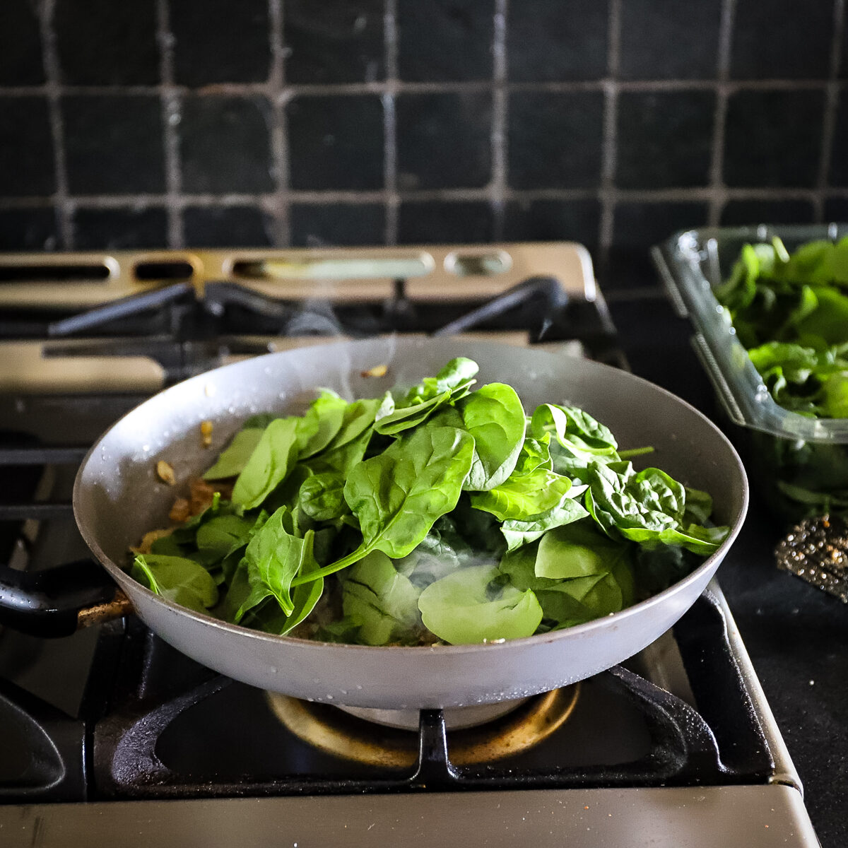 A heap of fresh baby spinach is added onto the pan of cooked onion. It is not all of the spinach, it is about ⅓ of it.