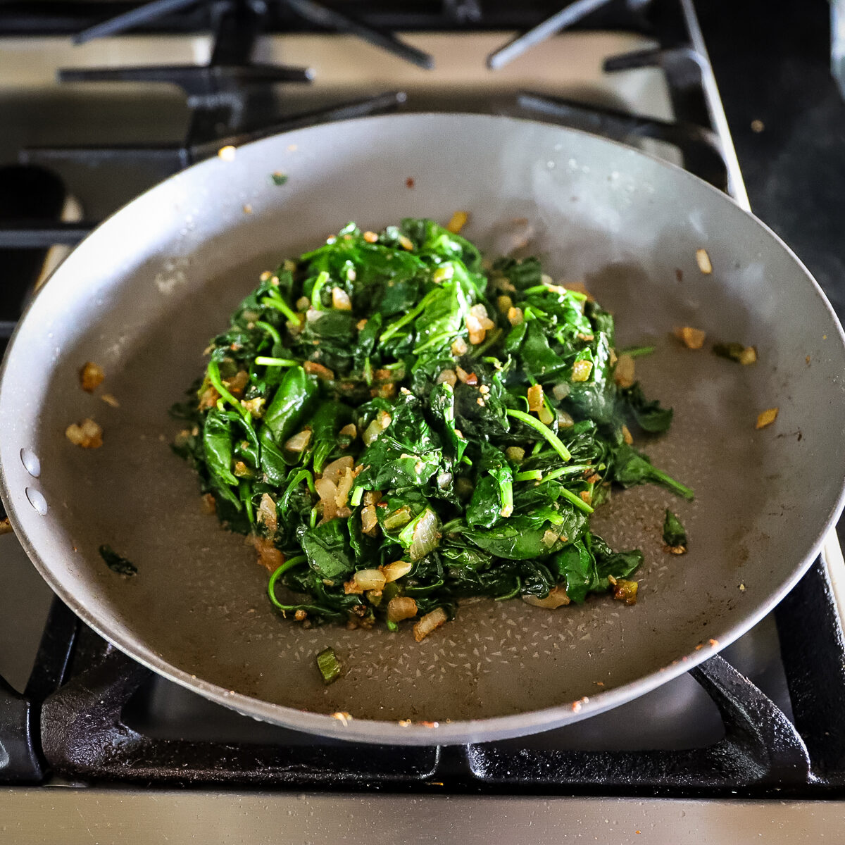 The spinach is all cooked and has shrunk down to a small percentage of it's original size. The bright green palak is piled in the center of the pan.