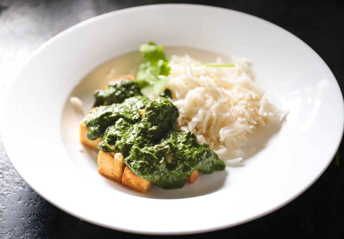 White bowl of rice and palak sauce over browned cubes of ofu.