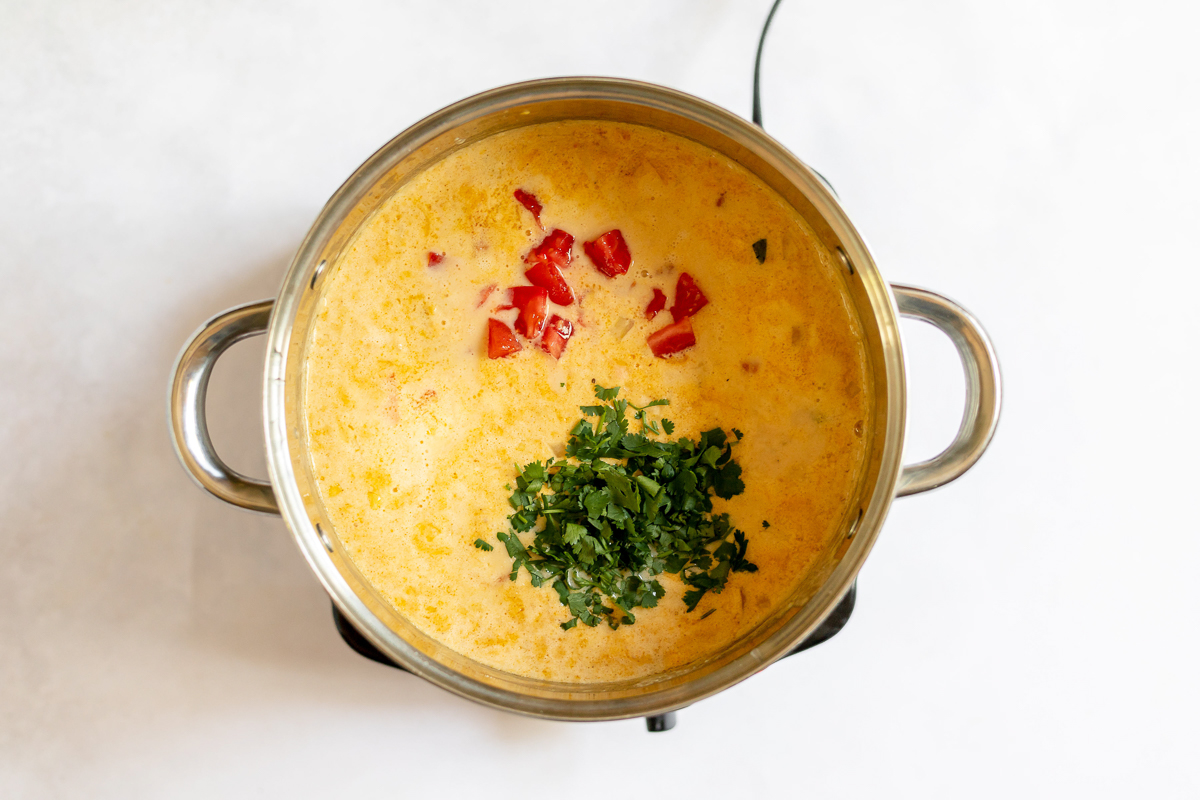 Soup is thick and creamy, a pale yellow orange color with some red tomato and chopped cilantro on top.