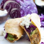 2 Soft tacos around a potato filling with purple cabbage and white crumbled cheese.
