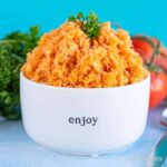 White bowl with the word 'enjoy' printed on it is filled with bright orange Spanish rice.