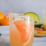 Peachy pink grapefruit drink with a grapefruit and lime wedge.