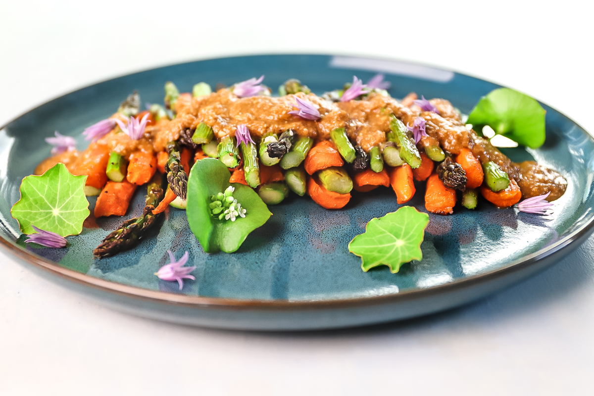 A closeup, side view of the carrot and asparagus goma salad. It is garnished with purple chive blossoms.