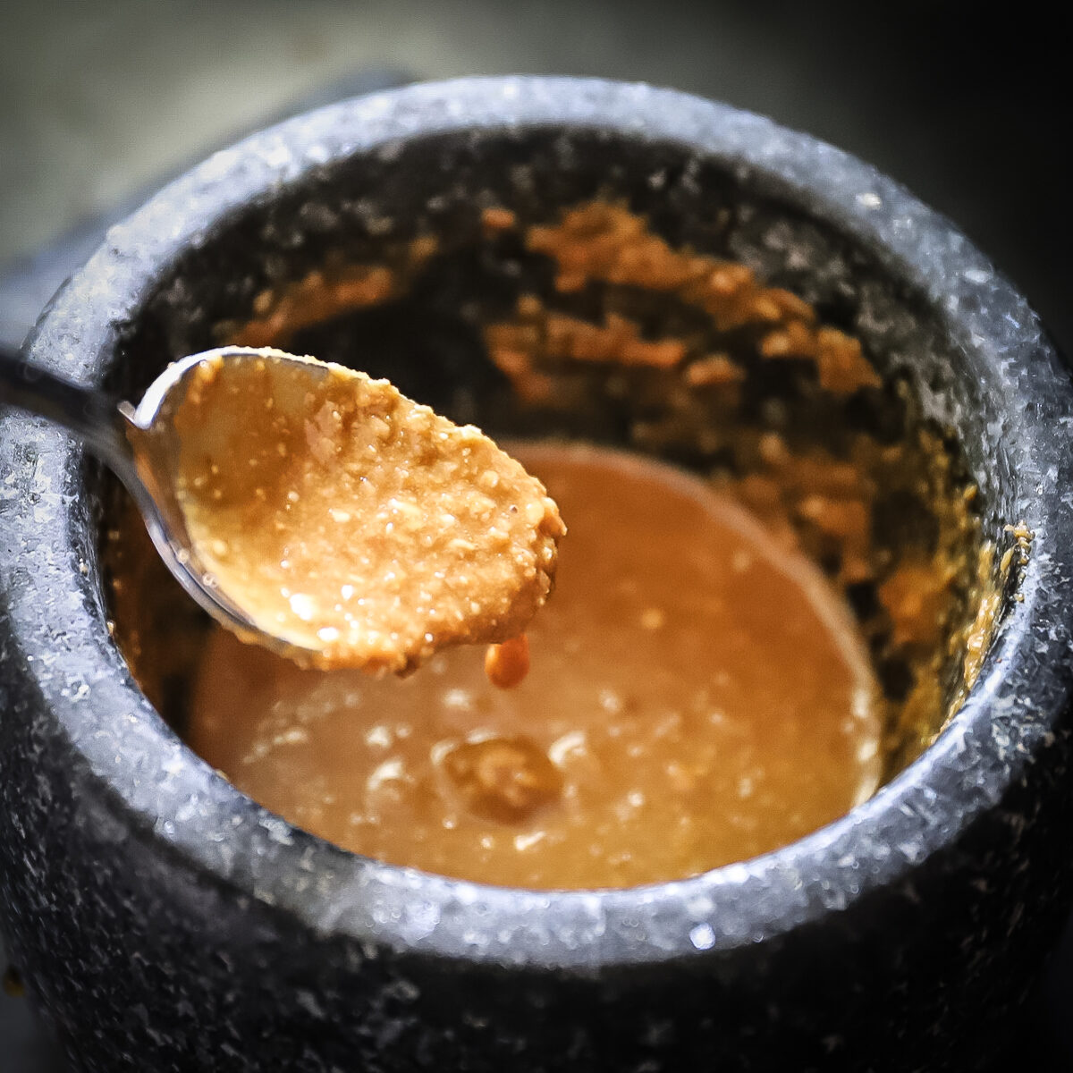 A spoon held up is dripping goma dressing to show the consistency of the sesame seed mixture.