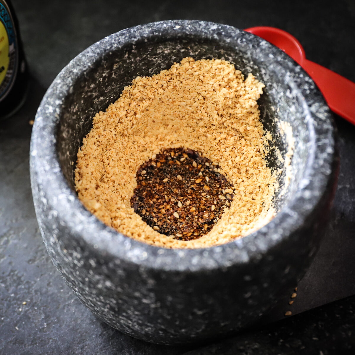 Dark brown soy sauce has been added to the center of the ground sesame seeds but not yet stirred in.