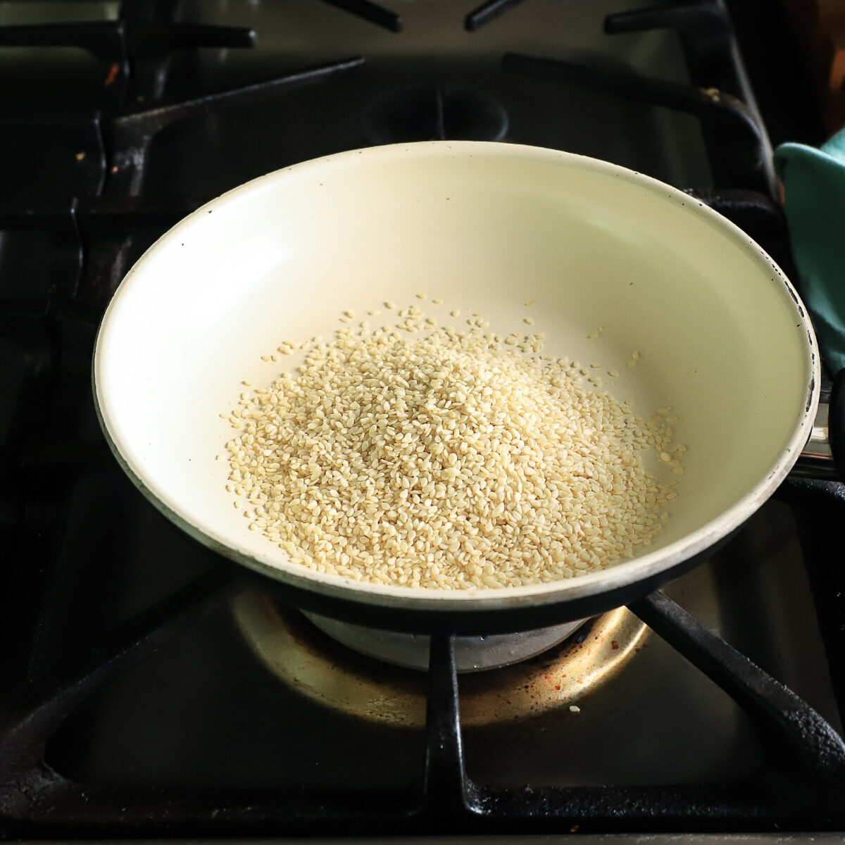 White sesame seeds in a white coated frying pan set on a stove.