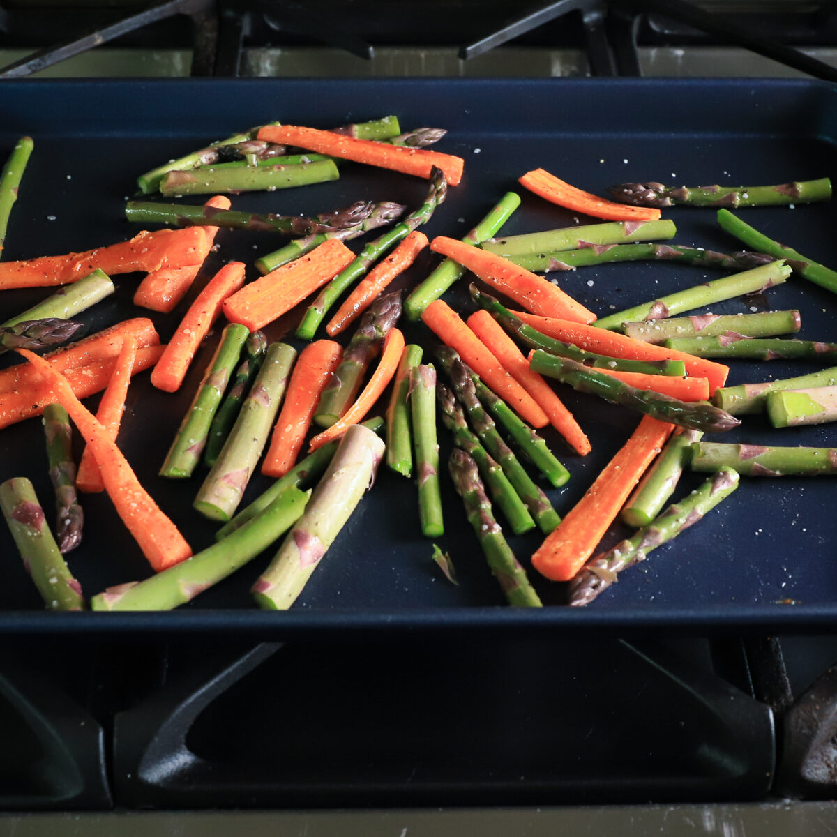 The cut carrots and asparagus are spread out on the dark blue baking sheet so they roast evenly.