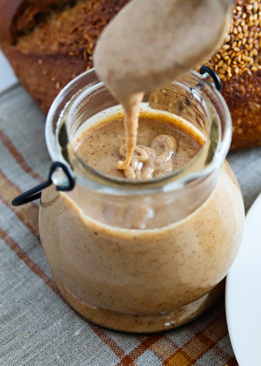Closeup of brown nut butter dripping off a spoon into the glass jar it's being spooned from.