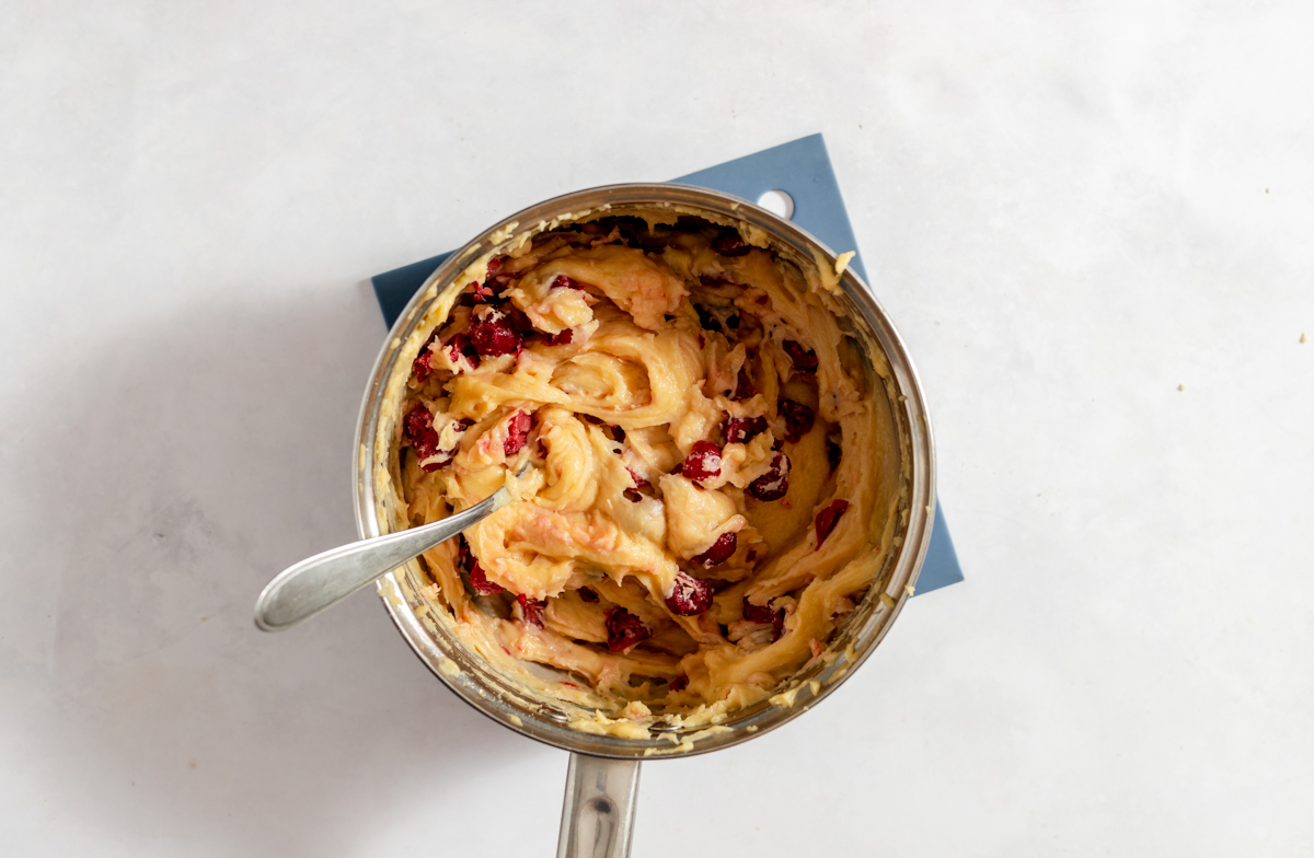 Cherries are gently stirred in to the batter with a spoon in the saucepan.