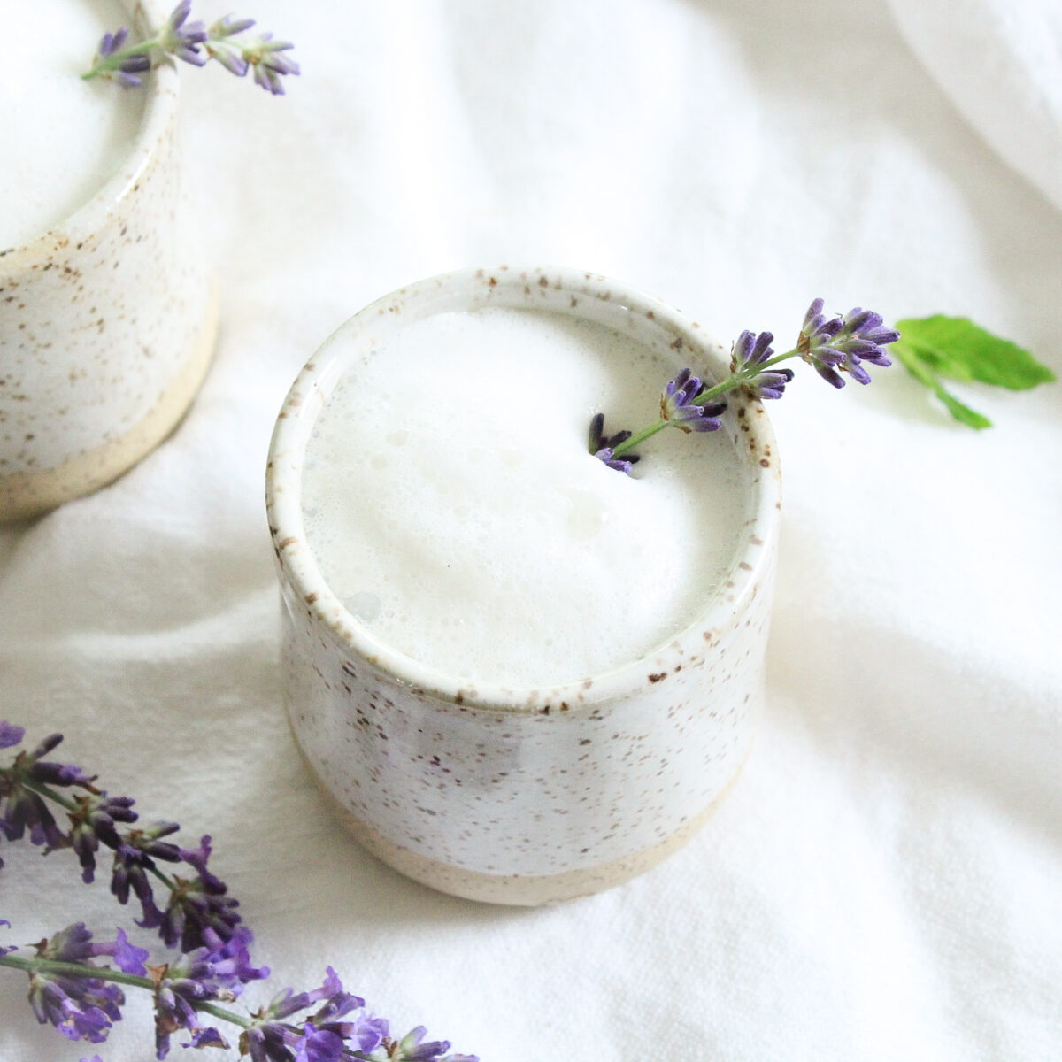 Cream pottery mug with foamy milk tea garnished with a sprig of lavender. 