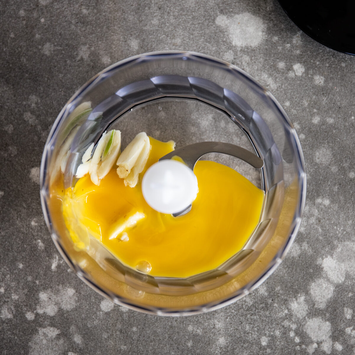 Deep yellow egg yolks and sliced garlic in the bowl of a small food processor.
