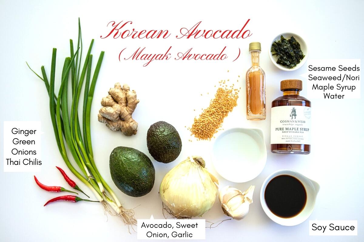 Overhead photo of the ingredients for Korean avocado with text labels for each. Ingredients include red thai chilis, scallions, ginger, avocado, onion, garlic, sesame seeds, vinegar, water , soy sauce, maple syrup and nori seaweed.