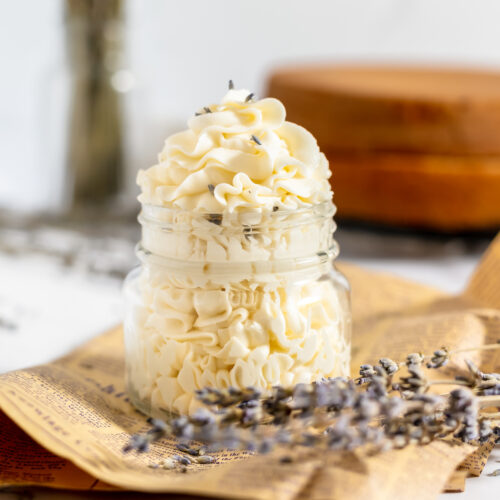 Creamy off white frosting piped into a glass jar with lavender buds sprinkled around.