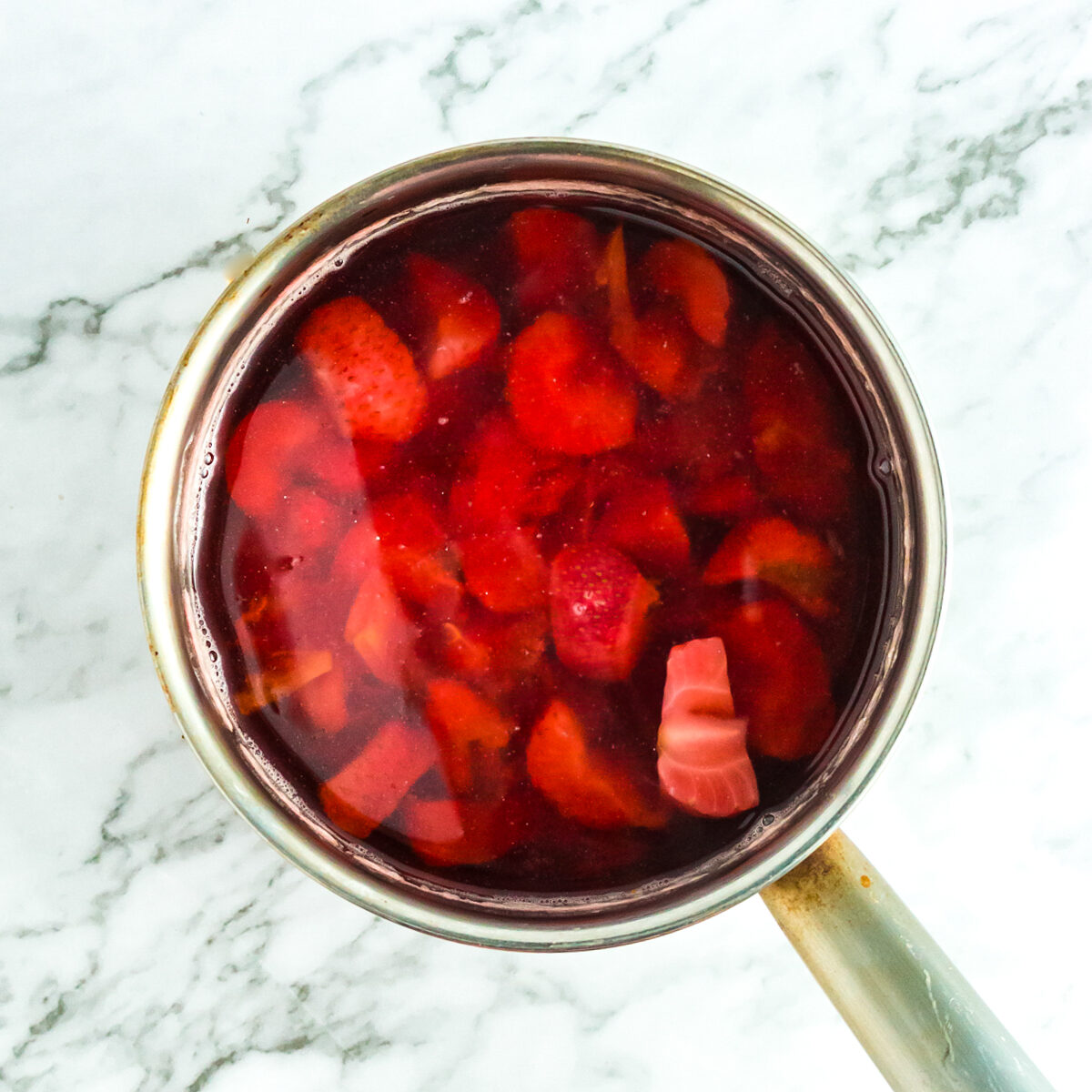 Sliced strawberries and peaches have been added to the simple syrup in the saucepan.