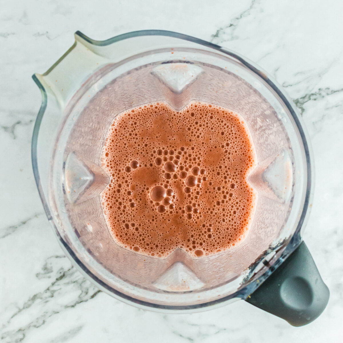 A blender cup on white counter with frothy pink juice in it.