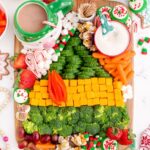 A wooden platter decorated to look like the green and brown buddy the elf sweater with broccoli, cheese cubes, carrots, marshmallows and grapes.
