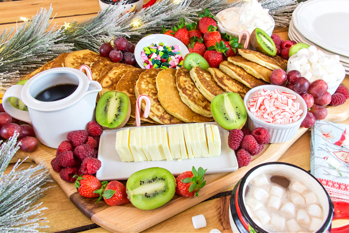 Green, red and white breakfast board with a heap of golden pancakes in the middle.