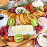 Green, red and white breakfast board with a heap of golden pancakes in the middle.