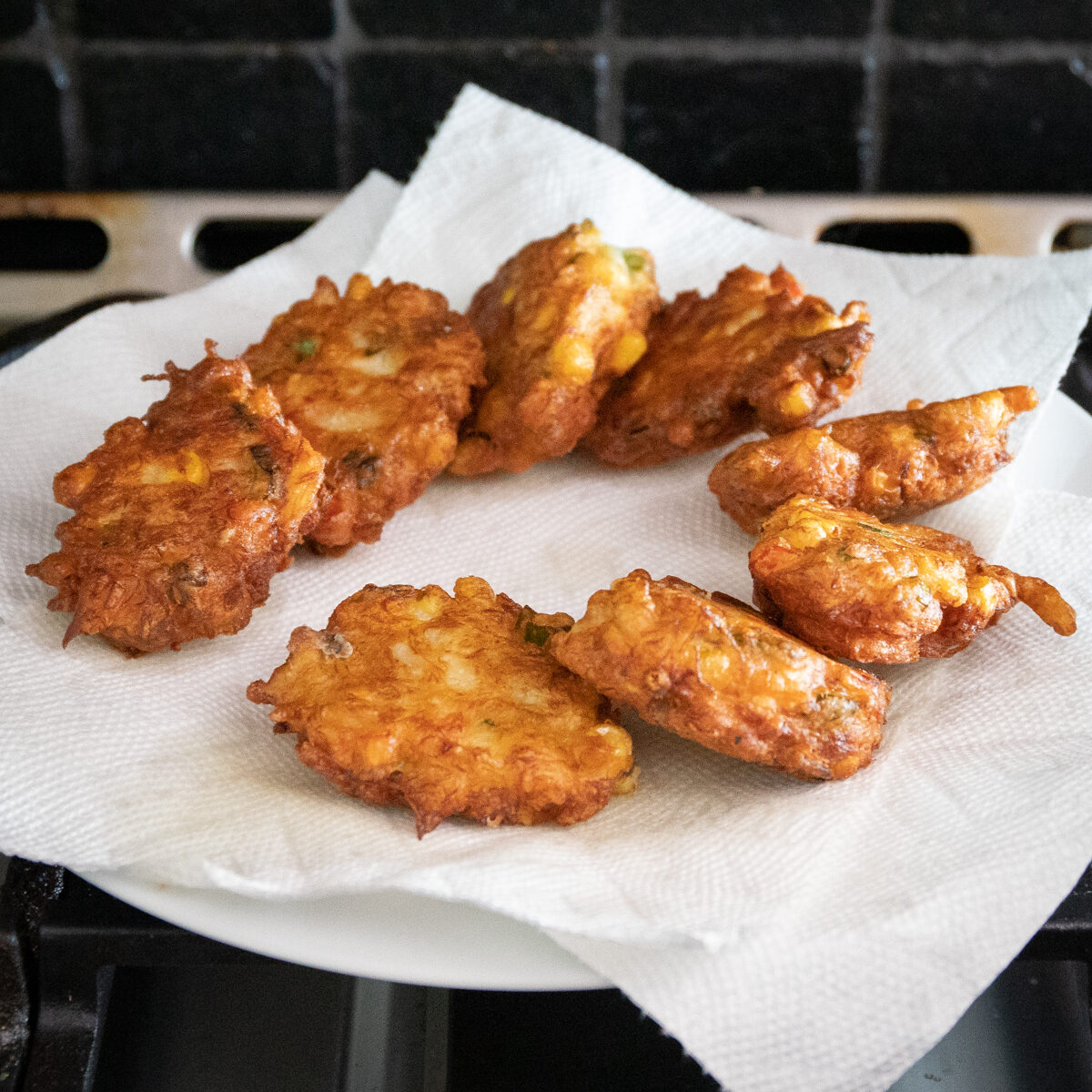 Eight golden brown crispy fritters are on a paper towel lined plate.