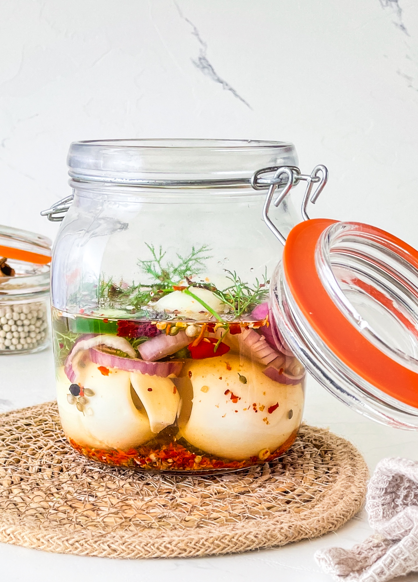 Pickled eggs in a jar with green herbs and red chilis.