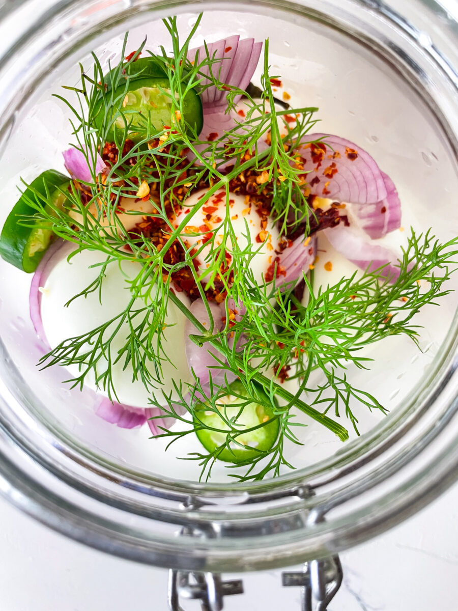 Top down view of mason jar stuffed with eggs, purple onion and dill fronds.