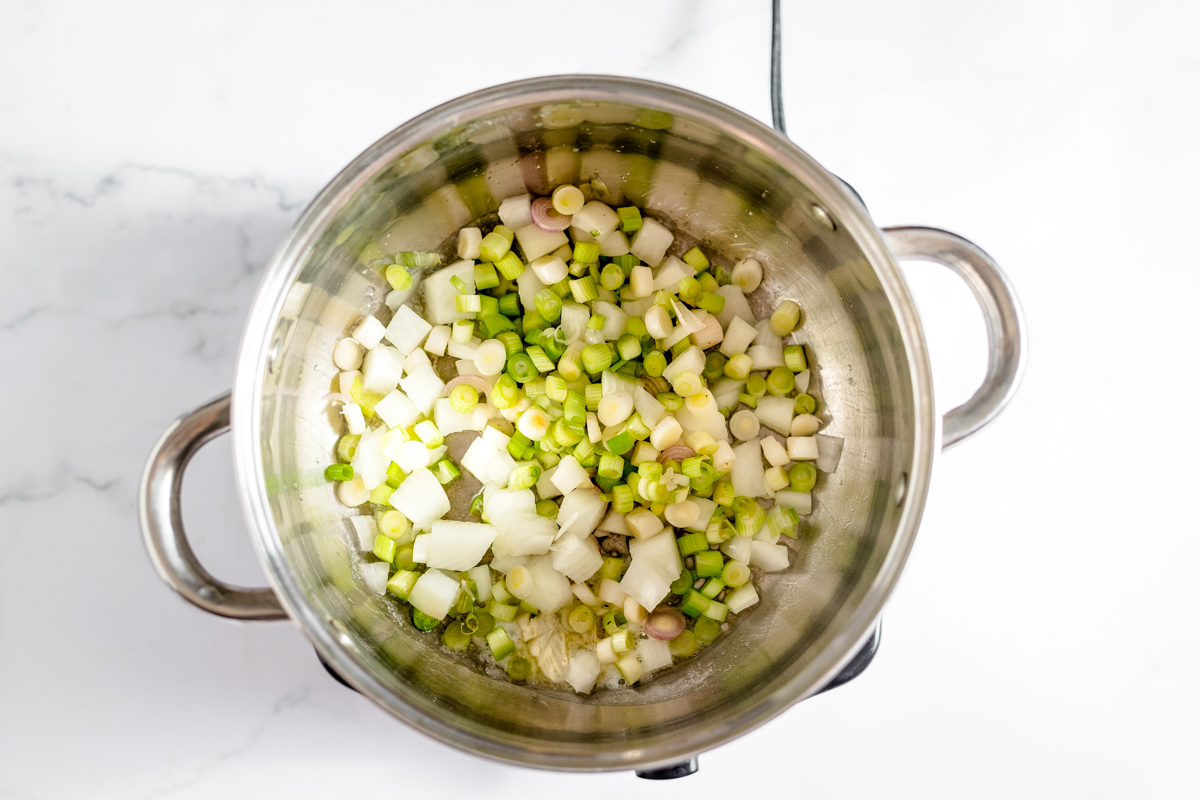 Pale green onions, garlic and shallots cooking in a stainless steel pot.