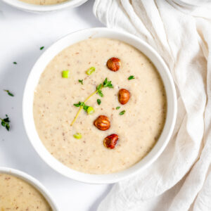 Creamy hazelnut soup in a white bowl garnished with thyme and hazelnuts.