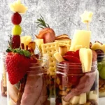 Open mason jars filled with meat cheese, crackers and fruit.