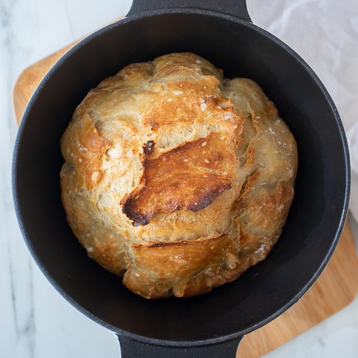 A round loaf of baked bread in a black cast iron Dutch oven.