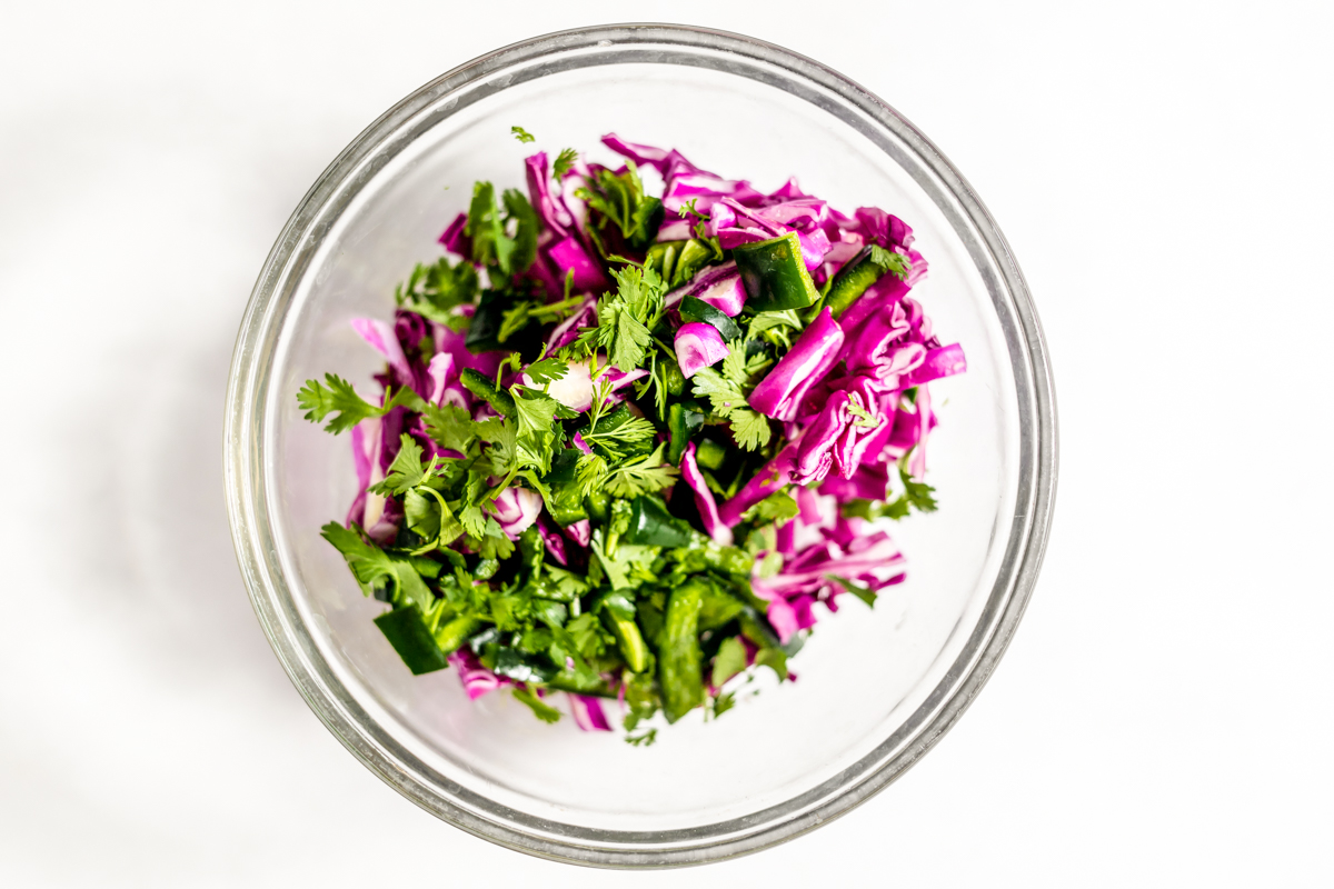 A clear bowl with purple cabbage, shredded cilantro and chopped green poblano peppers.