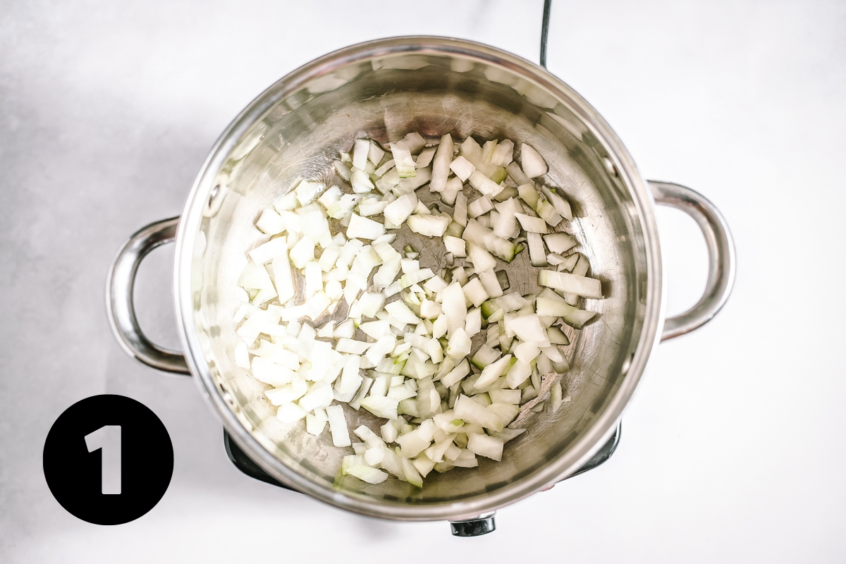 Silver pot with chopped onions sautéing in oil.