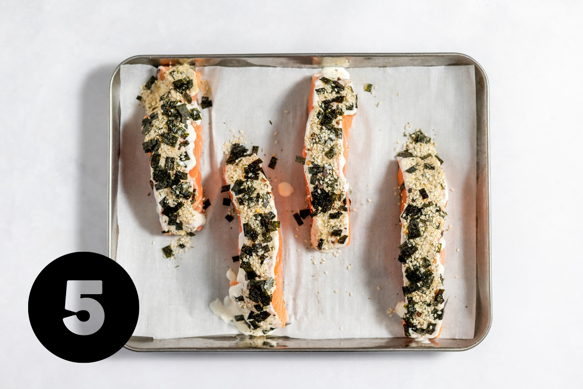 Parchment paper lined baking tray with 4 rectangular pieces of salmon covered in crumbled seaweed and sesame seed mixture.