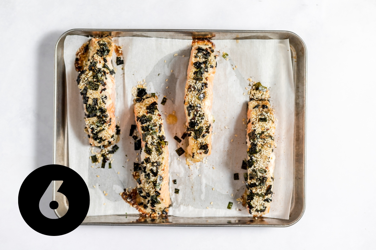 Parchment paper lined baking tray with 4 rectangular pieces of salmon covered in white mayonnaise mixture that has been baked and is lightly browned around the edges of each piece.