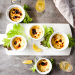 Finished baked oysters mornay served with lemon wedges and lettuce leaves. Served with glasses of white wine.