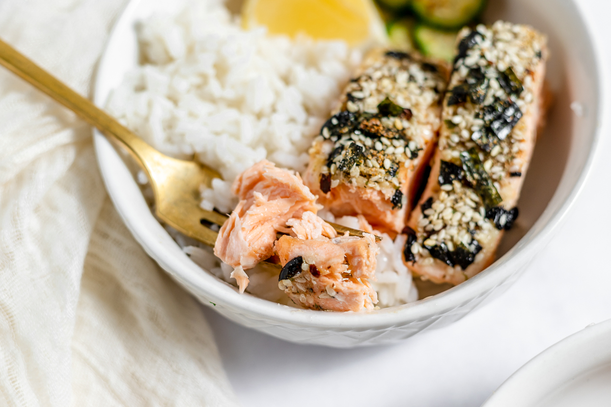Bowl of furikake topped salmon on rice with cucumber and lemon as garnish.