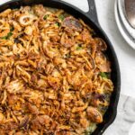 A green bean and mushroom casserole topped with crispy fried onions in a black cast iron pot.