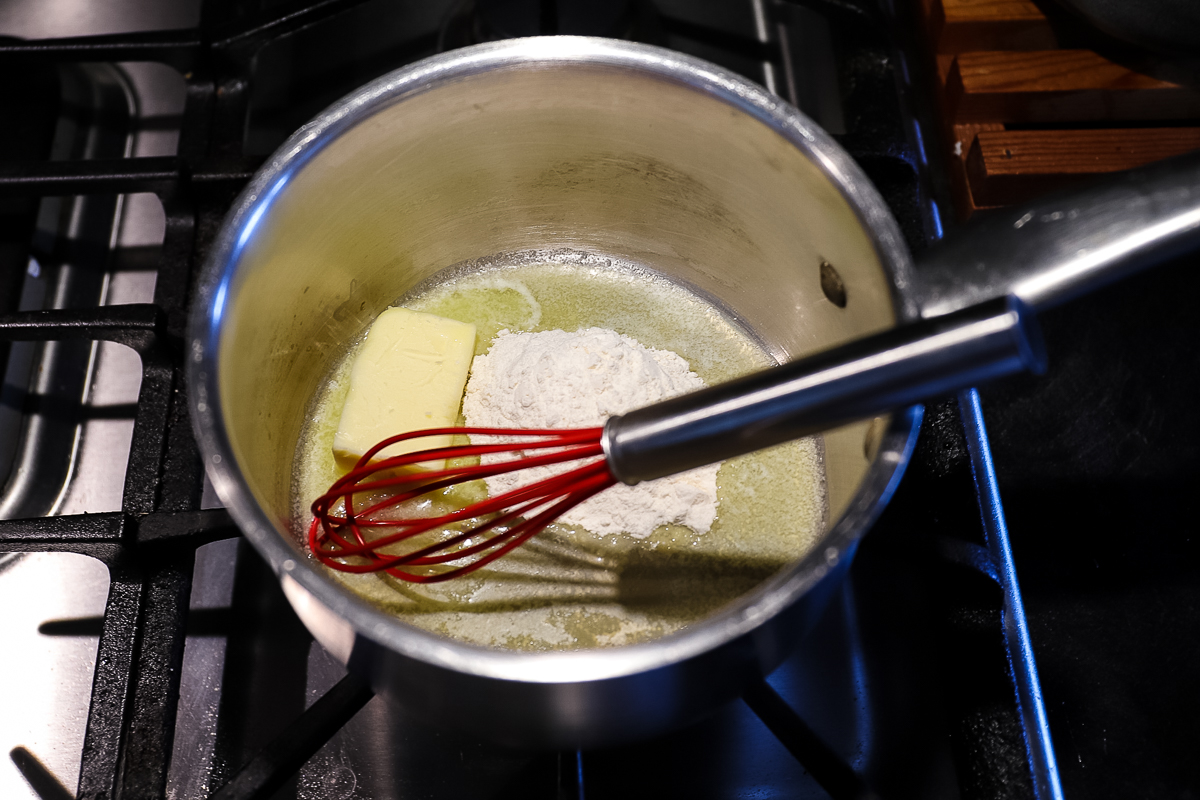 Stainless steel pot with butter starting to melt and a small pile of flour on one side.