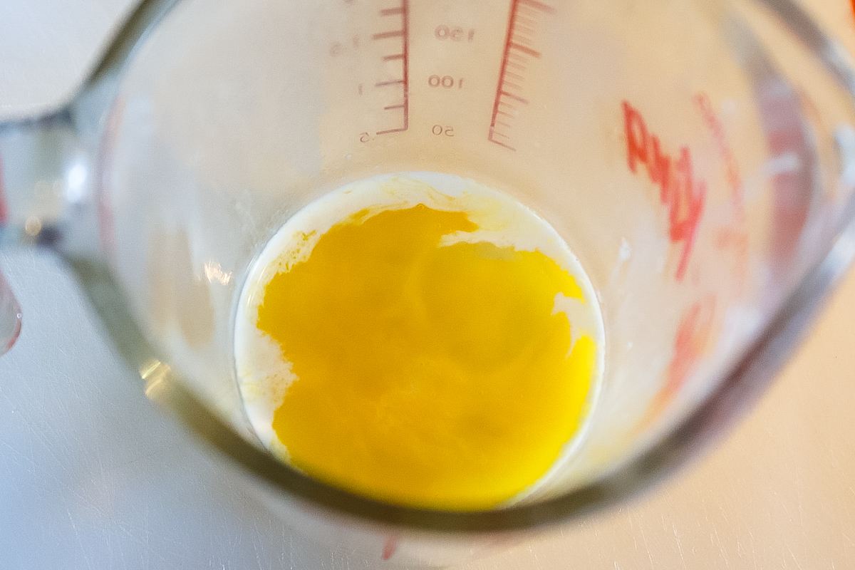 A measuring cup has egg yolk and a tablespoon of cream in it, not yet mixed.