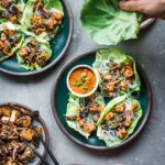 Lettuce wraps filled with tofu and mushrooms with a dish of orange sauce on the side.