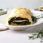 Puff pastry oval filled with green, brown and white spinach and mushrooms.