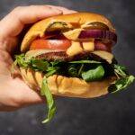 Juicy burger with vegan cheese, mushroom, lettuce and tomato held in a hand.