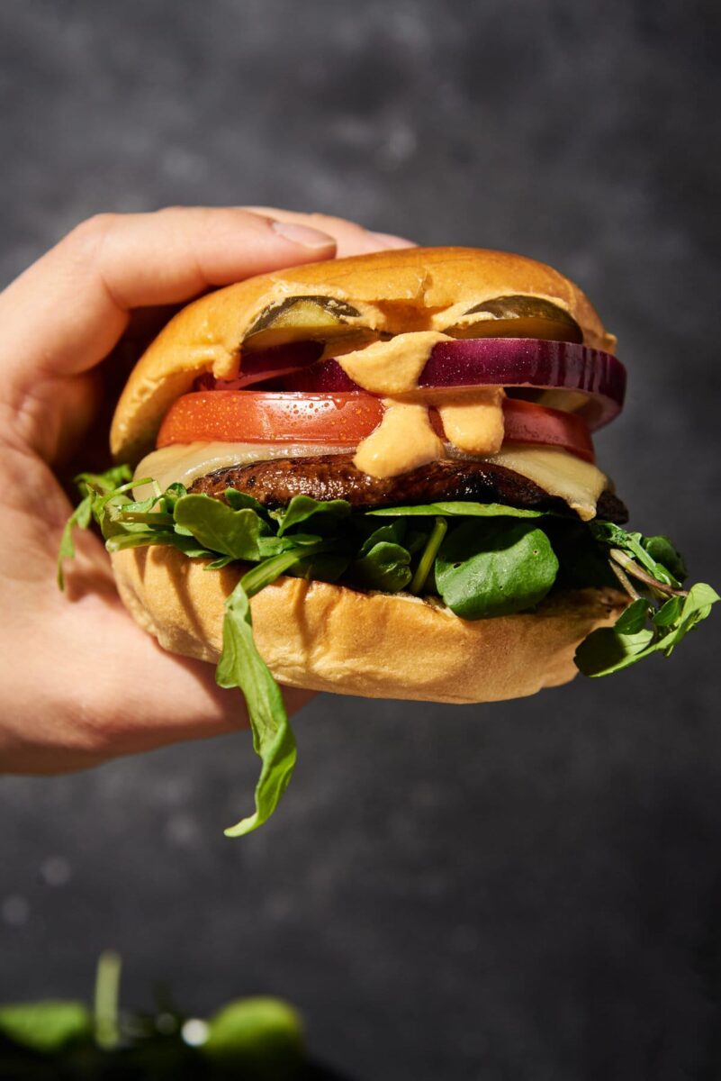 Juicy burger with vegan cheese, mushroom, lettuce and tomato held in a hand.