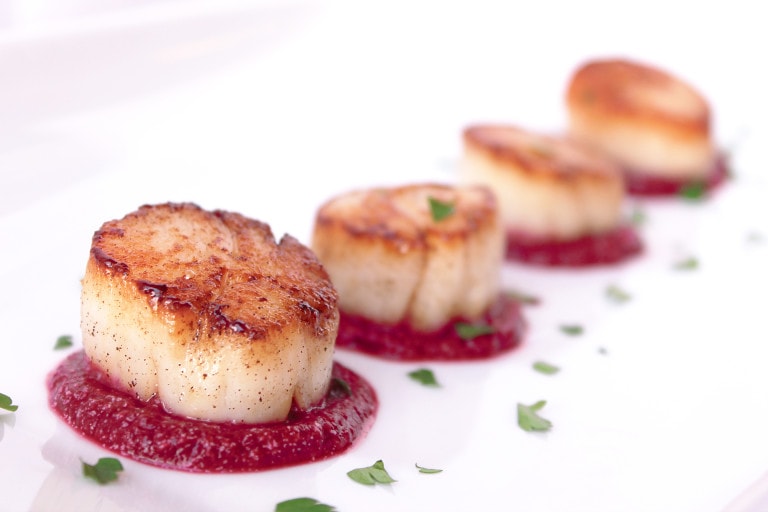 Row of caramelized scallops on top of small circles of red beet puree on a white plate.