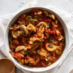 Mexican tomato mushrooms with bell peppers in a white round casserole on white table.