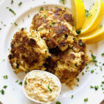 Fried lion's mane cakes are browned and crispy with lemon wedges and a creamy sauce on the side.